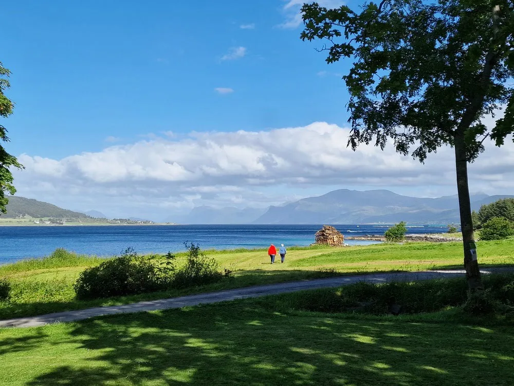 A couple walking across a green field with the sea in the background