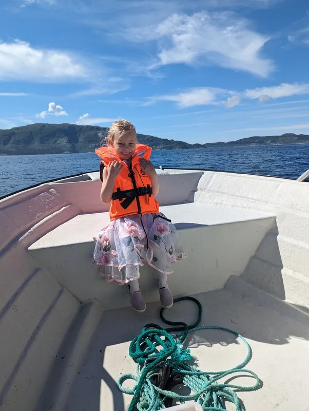 A girl in a life jacket in front of a small boat