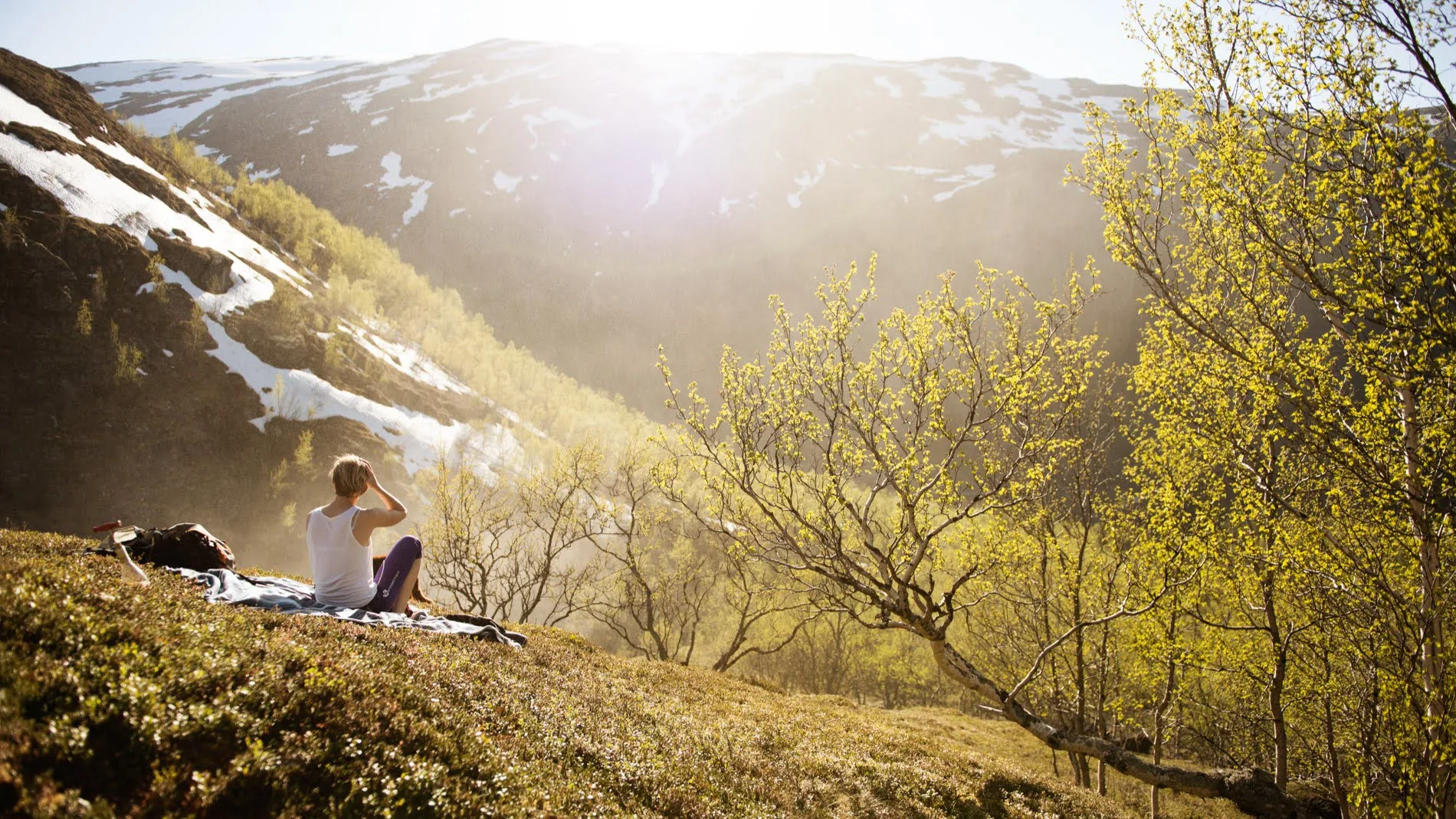 A person relaxing on a blanket with a view of green mountains with snow on top