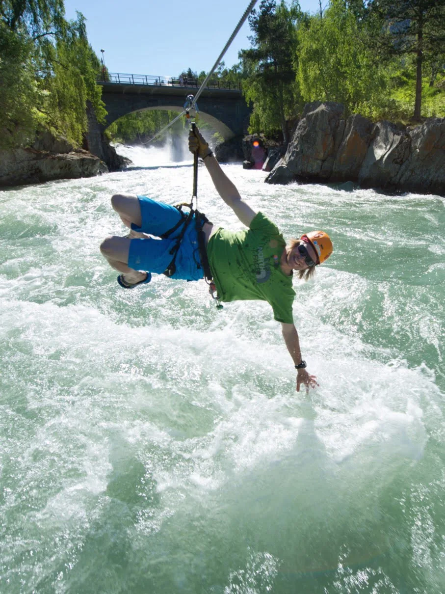 A person hanging from a zipline with his hand down into a powerful river