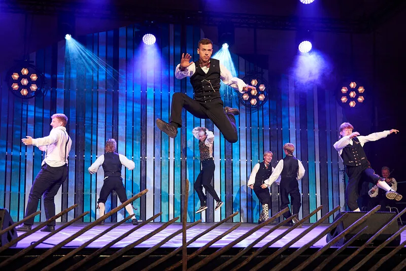 Young dancers in traditional Norwegian costumes perform energetic jumps on stage during a colorful folk dance performance in Lom
