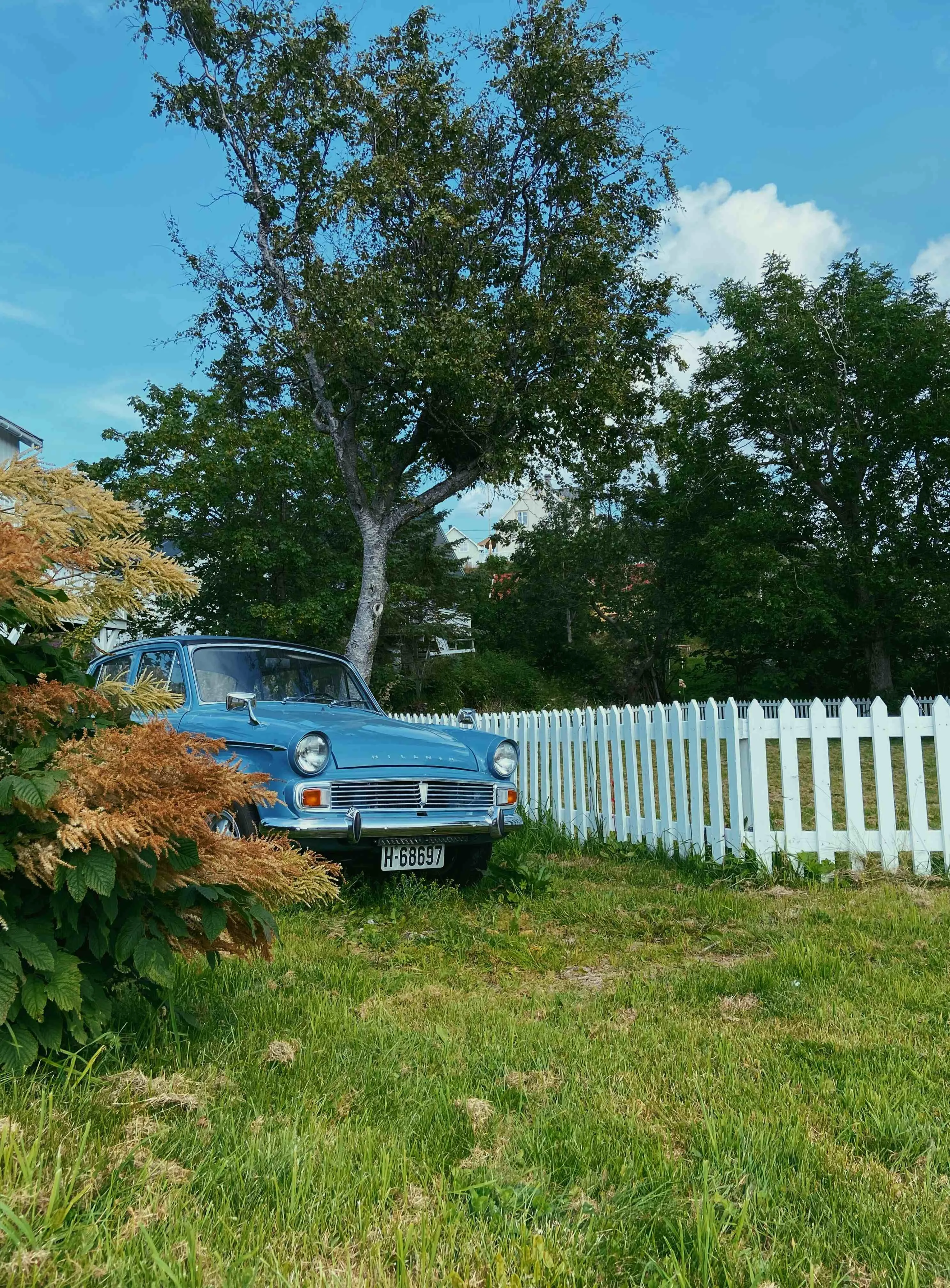 Street scene in Sørvågen with a blue car beside a white wooden fence