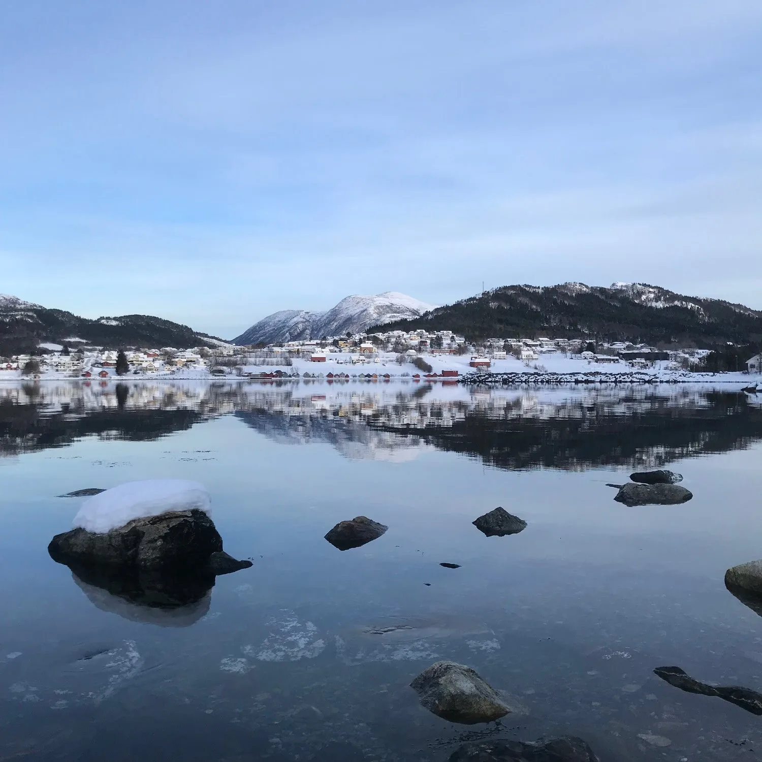 Tennfjord village by the fjord with green fields and mountains under a clear sky
