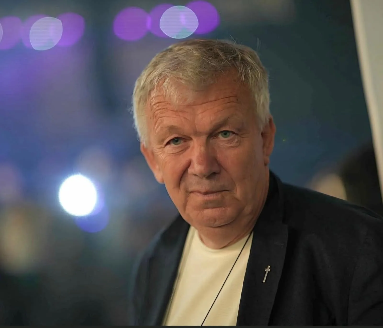Close-up portrait of Arnt-Ove Tenfjord wearing a dark jacket, with purple and white bokeh lights behind him