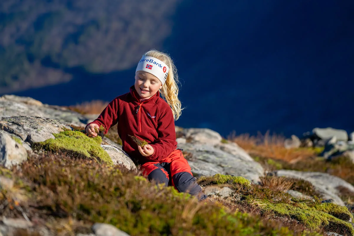 Young girl in red outdoor clothes sitting and smiling on a mountain, surrounded by rocks and heather