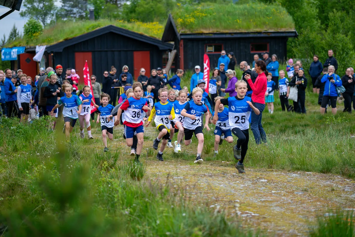 Children's race in Tomrefjord with excited kids sprinting from the start line, supporters and red and blue cabins in the background